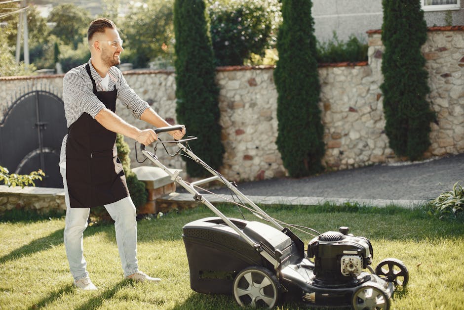 A man using a lawn mower to trim grass in a sunny outdoor garden.